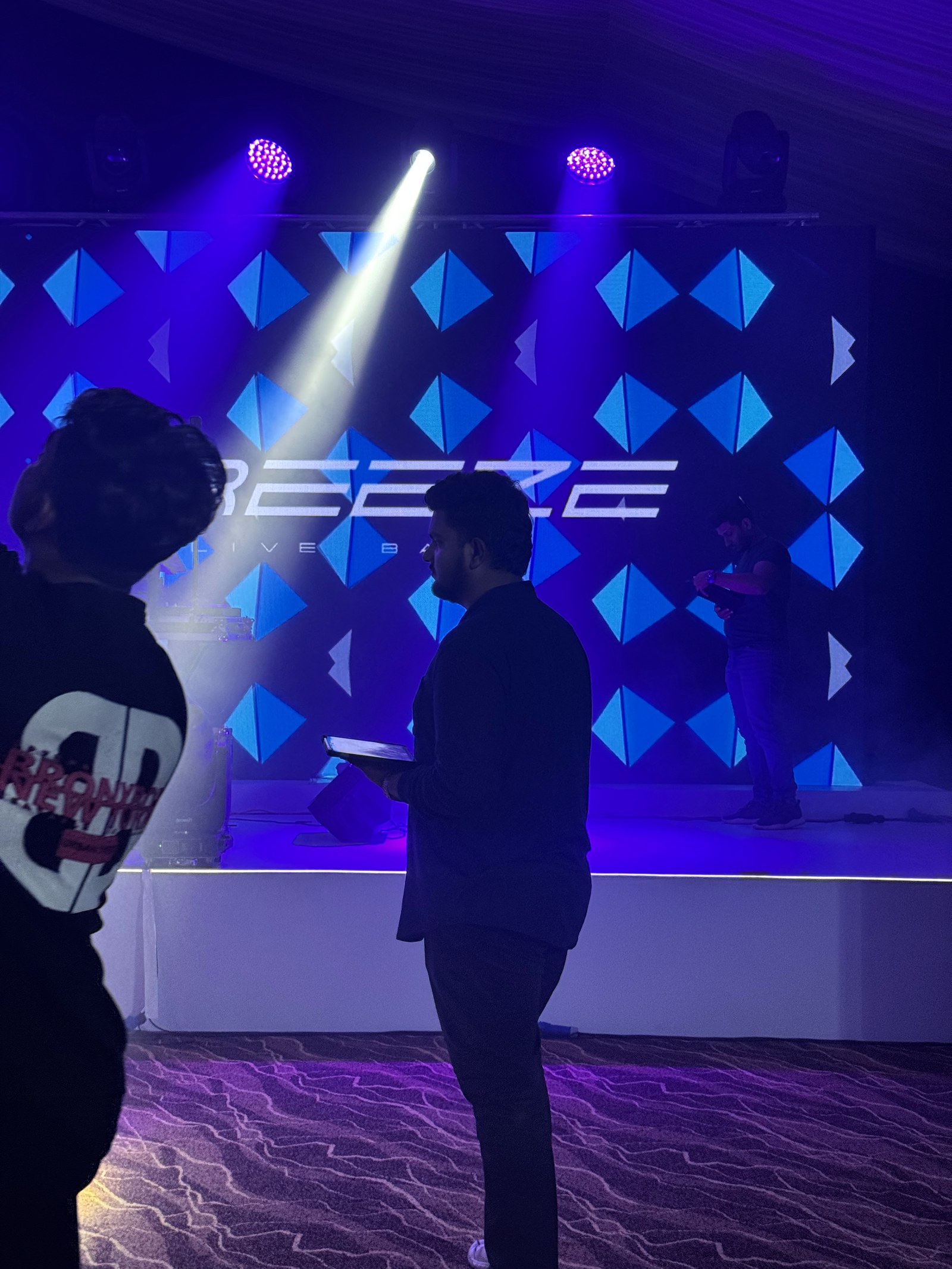 Crew member filming a presenter on stage in front of a branded event backdrop