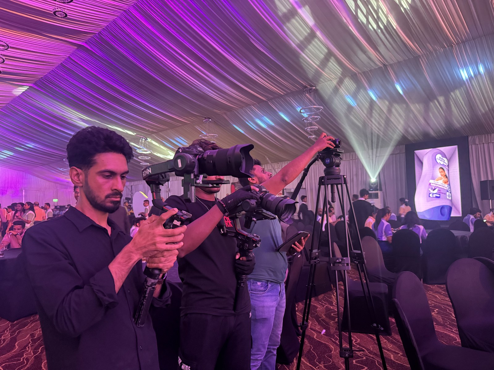 Multiple camera operators with tripods covering the stage during an event